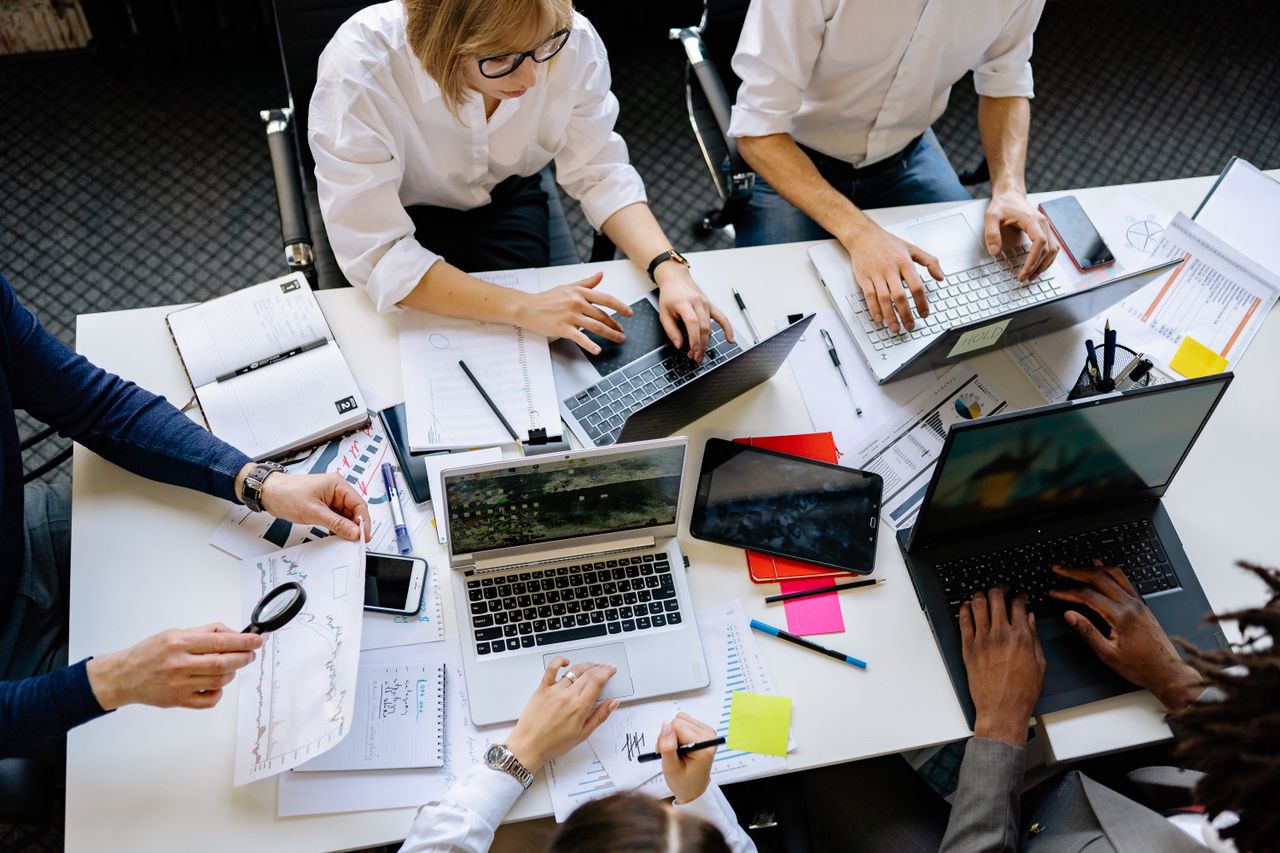 Vue en plongée d’une équipe d’entreprise collaborant avec des ordinateurs portables et des documents.